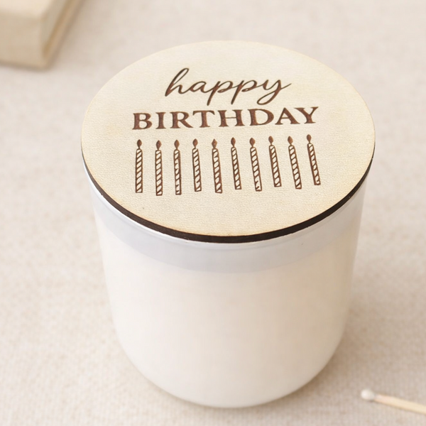 White candle with a wooden lid featuring 'happy birthday' and candles on a light background