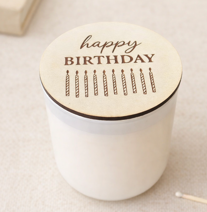 White candle with a wooden lid featuring 'happy birthday' and candles on a light background